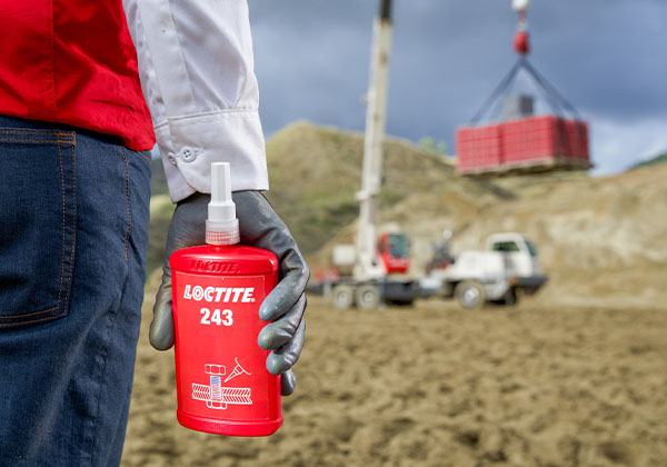 A person holding a bottle of LOCTITE in front of a crane.